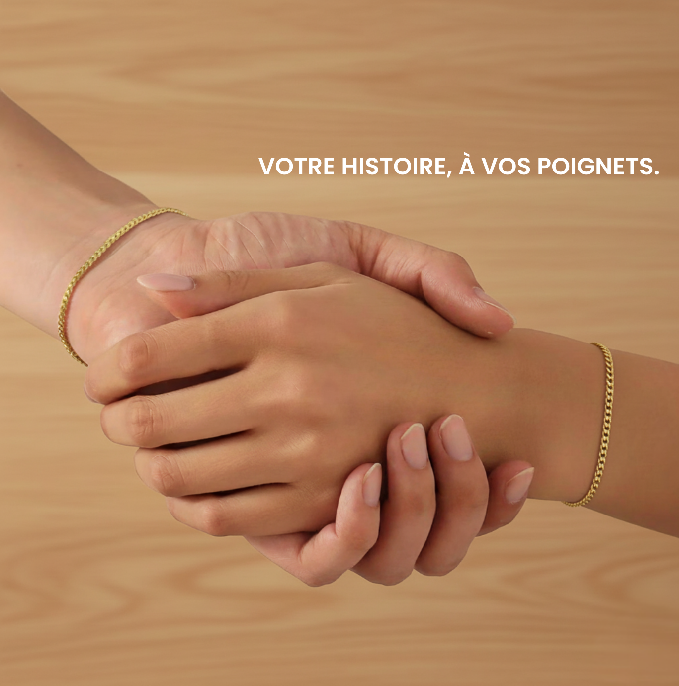Deux poignets ornés de bracelets dorés personnalisés se tiennent la main, fond bois clair.