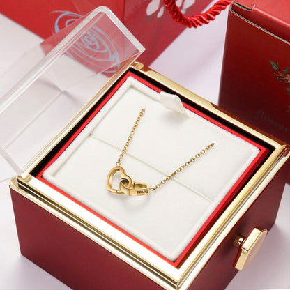 Coffret cadeau rose éternelle rouge ouvert révélant un collier doré avec deux cœurs gravés de prénoms.