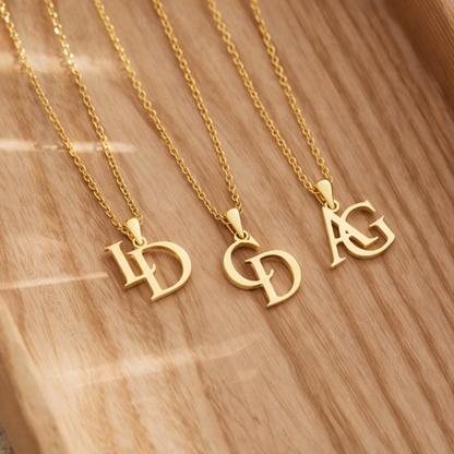 Sélection de trois colliers couleur or personnalisés initiales disposés sur une table.